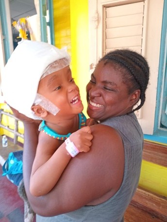 Baby Joe smiling in a caregiver's arms after receiving surgery in Haiti